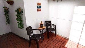 A small, enclosed patio area with two black plastic chairs, a small wooden table, and a hanging plant.