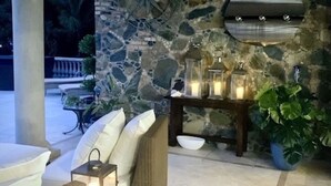 A stone wall with a round mirror, wicker furniture, and a lantern. - Welcome to your island home, Mystical Mermaid! (Cruz Bay)