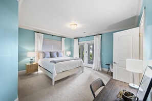 Relax in this serene bedroom with a large bed, nightstand, and table, offering a peaceful retreat with a door leading to an outdoor area.