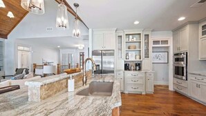 A spacious kitchen with marble countertops, stainless steel appliances, and white cabinetry.