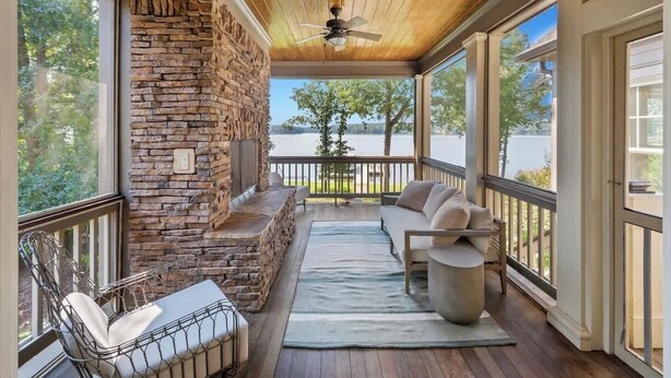 A covered porch with stone walls, a ceiling fan, and a view of a lake.