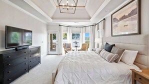A bedroom with a large bed, a TV, a dresser, and a painting on the wall.