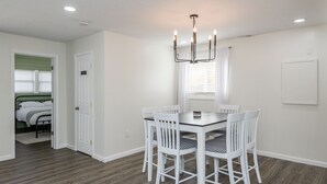 A dining area with a white table and chairs, a chandelier, and a view of a bedroom with a bed and green walls. - Central Location- Updated 3 Bed 2 Bath (Xenia)