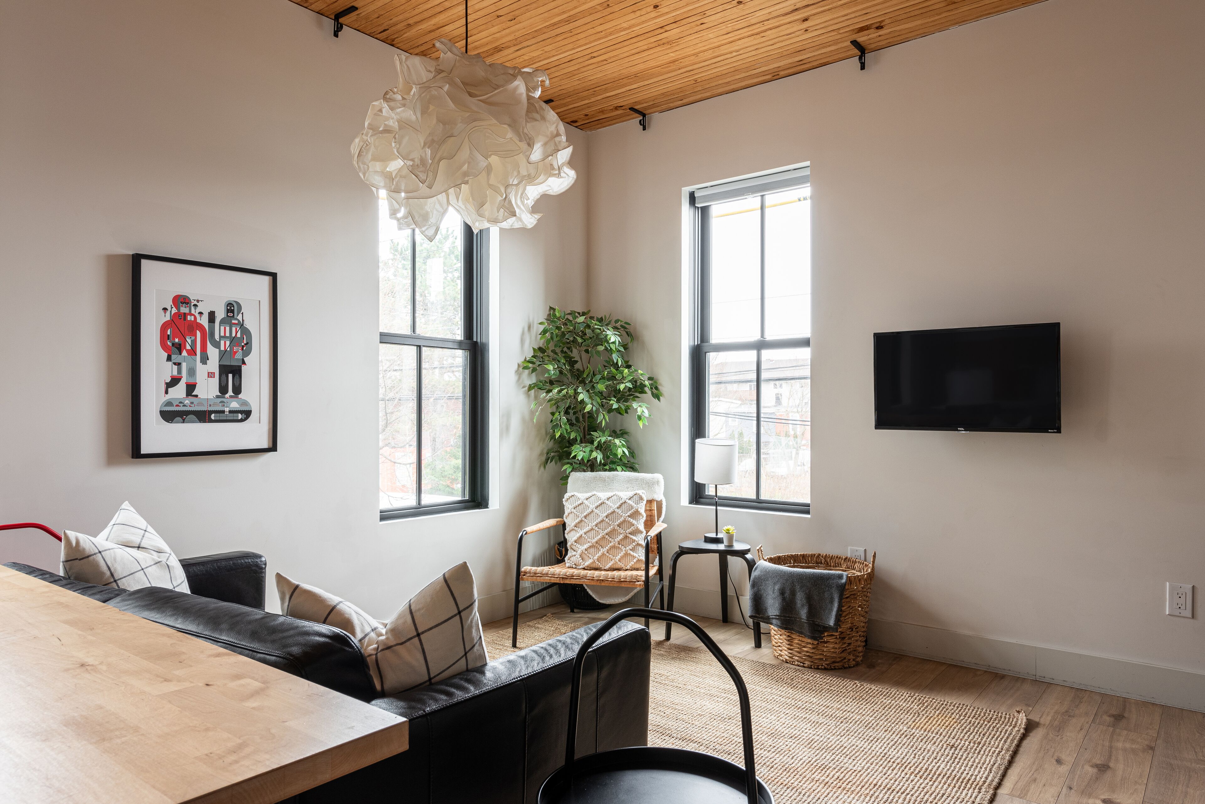 Una sala de estar moderna con techo de madera, un ventanal grande, un televisor de pantalla plana, una mesa de comedor y un área de estar confortable.