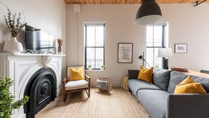A living room with a fireplace, sofa, and armchair. There are windows, a lamp, and a framed picture on the wall. - Brewery Park Hotel (Halifax)