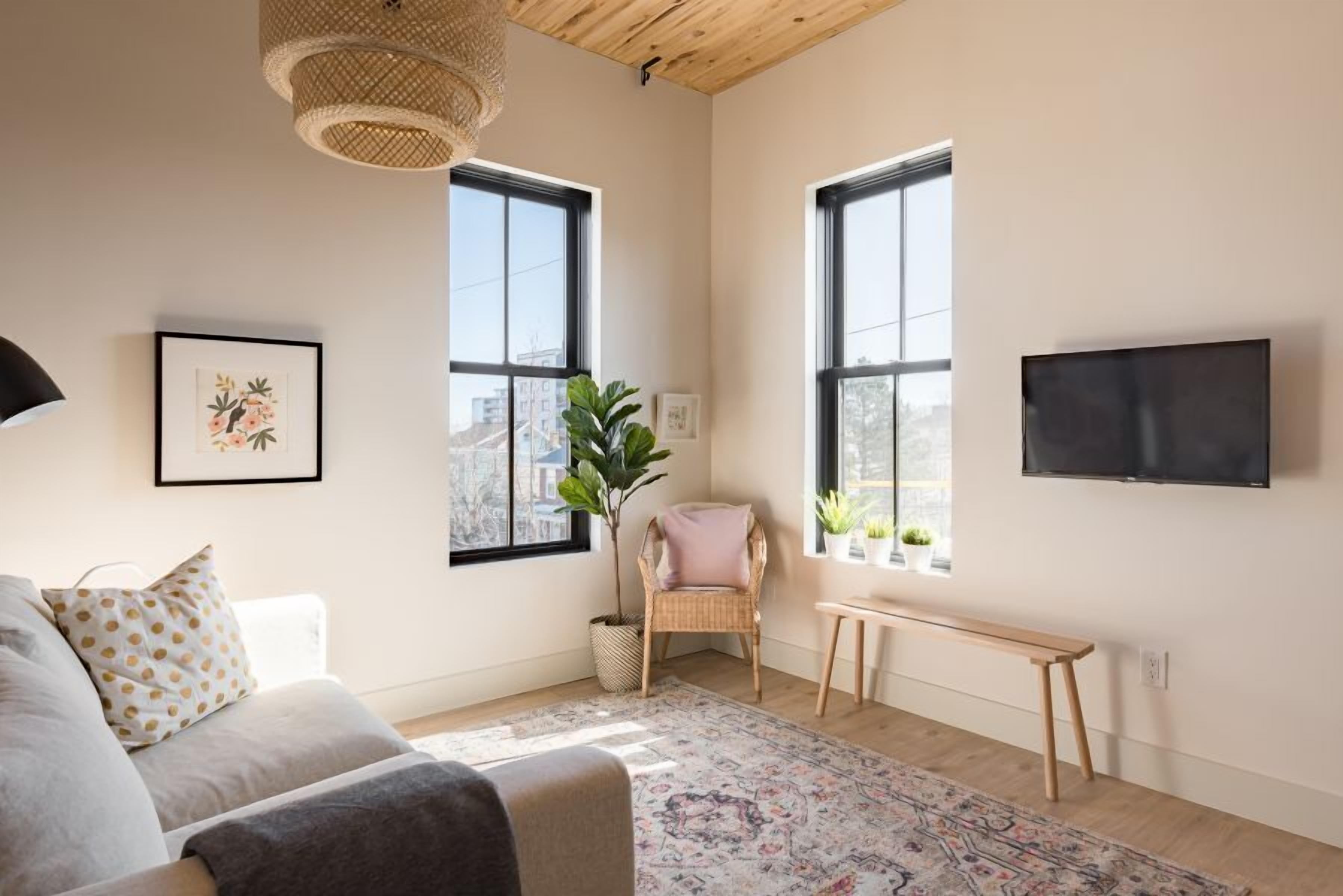 A modern living room with a sofa, a chair, a bench, a large window, and a flat-screen TV mounted on the wall.