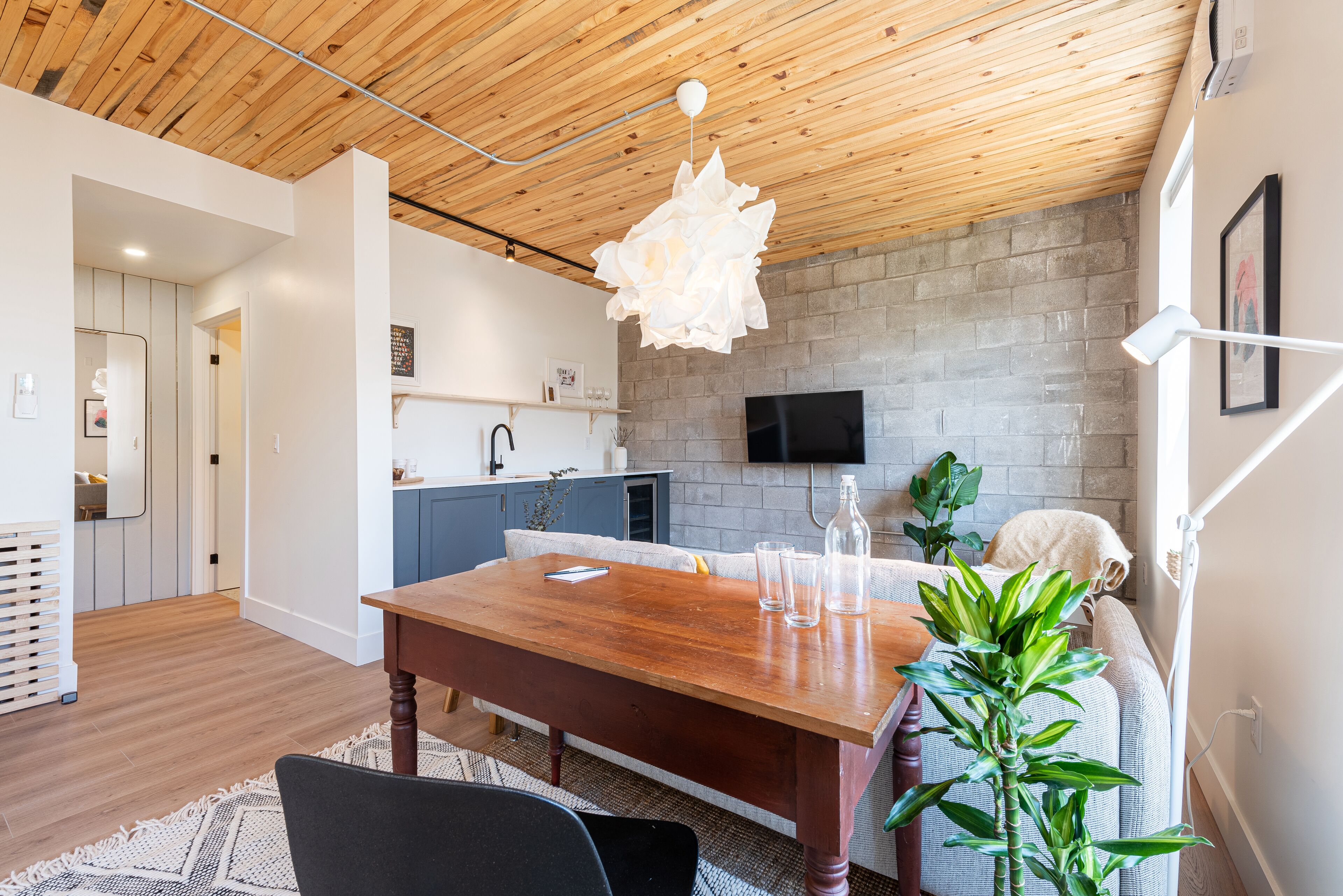 Une cuisine moderne avec un mur en pierre, un plafond en bois et un coin repas comprenant une table et des chaises en bois.