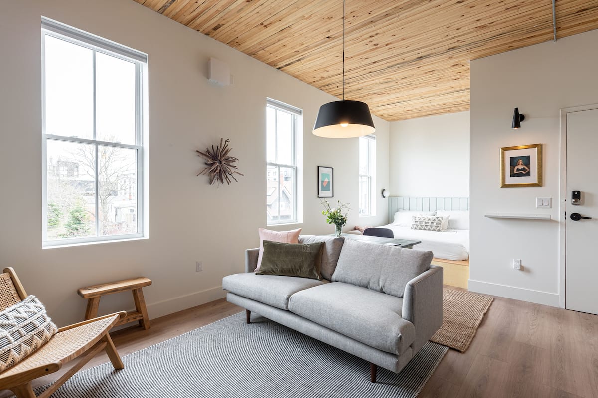Una sala de estar moderna con un sofá gris, un banco de madera y un ventanal grande.