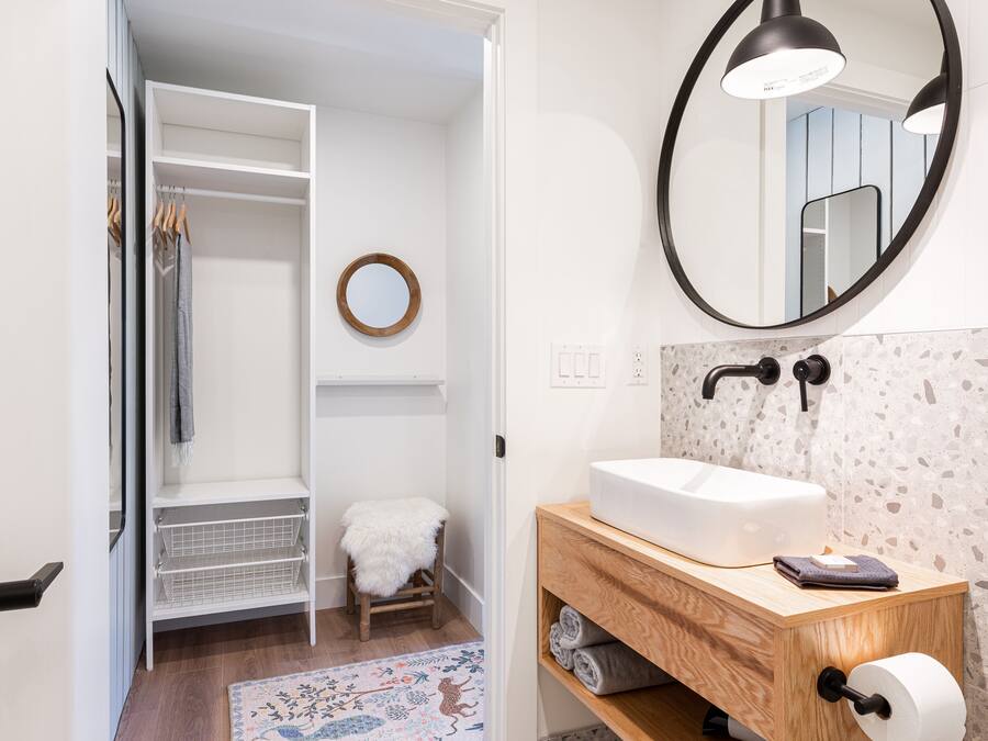 Een badkamer met een witte wasbak, houten wastafelmeubel en een ronde spiegel.