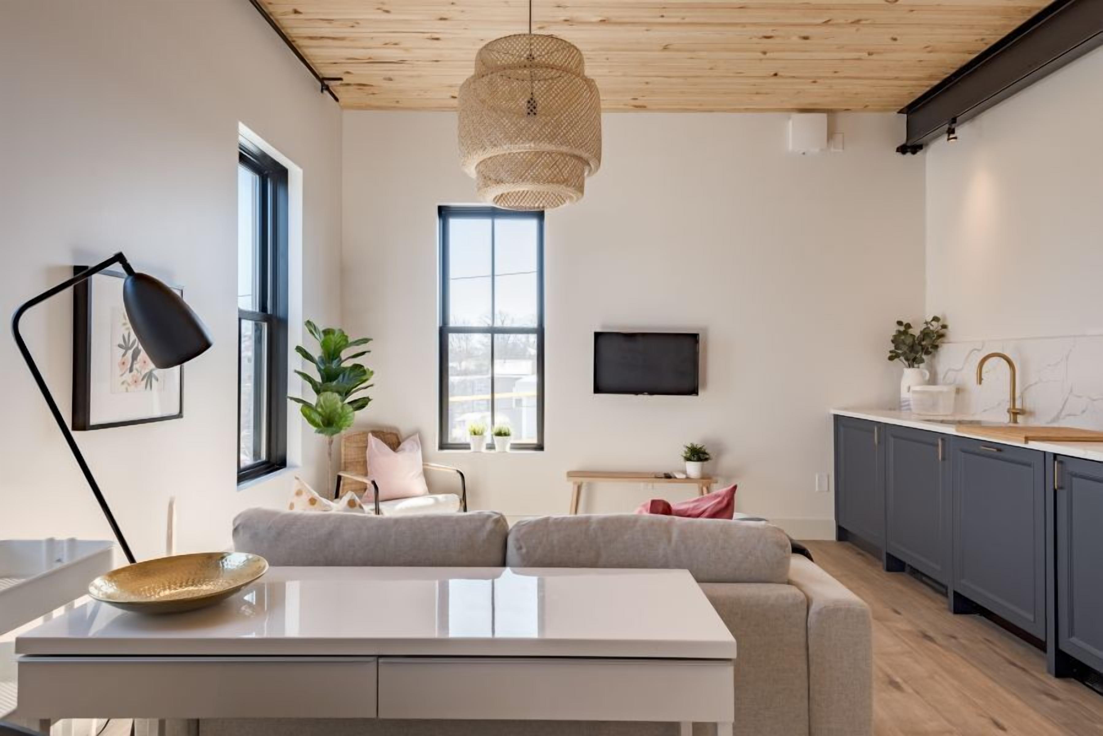 Una sala de estar moderna con un sofá, una mesa de centro y un televisor. Hay una zona de cocina con armarios y un fregadero.