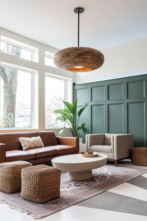 A modern living room with a brown leather sofa, a grey armchair, a round coffee table, and a woven pouf. - Brewery Park Hotel (Halifax)