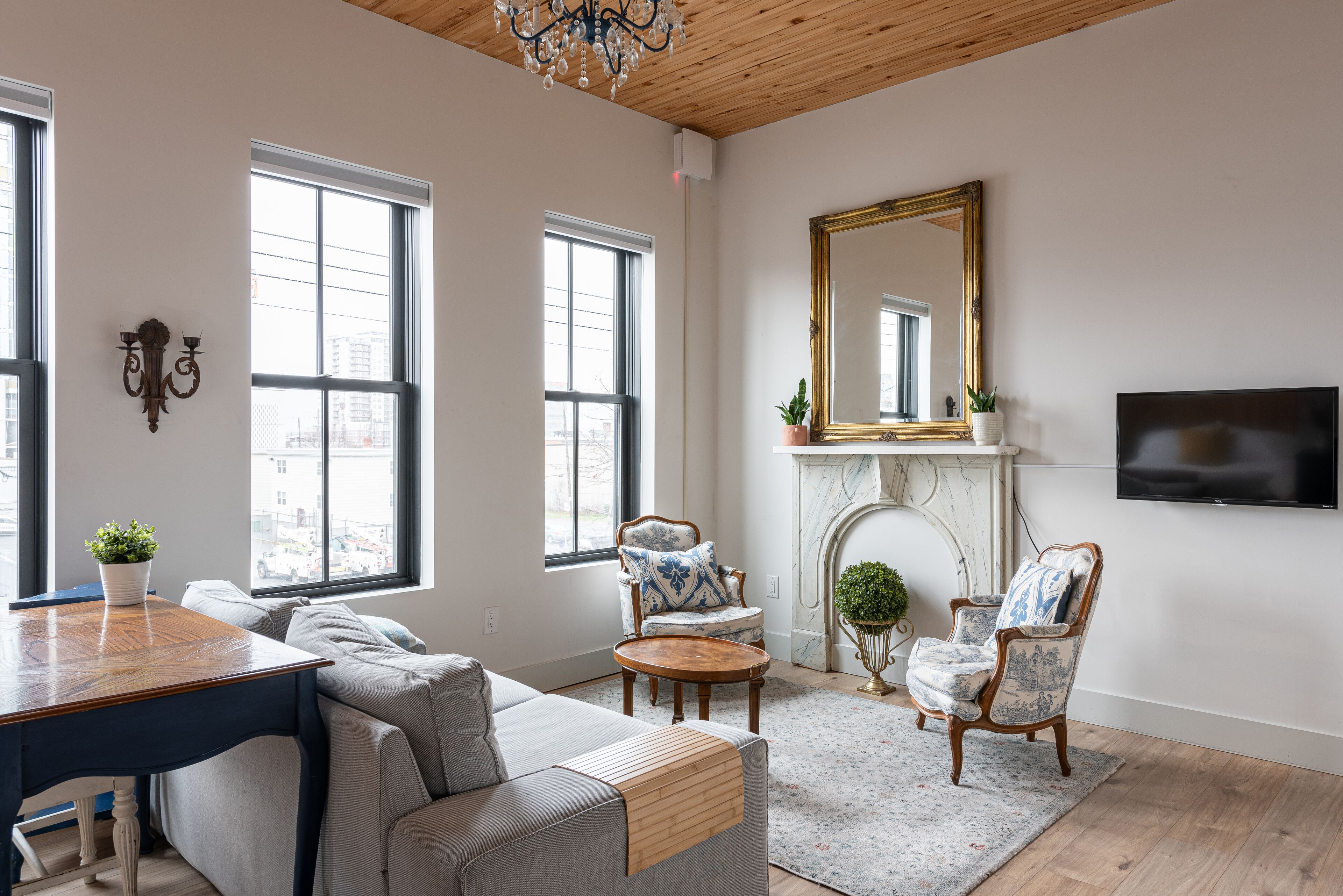A living room with a wooden ceiling, large windows, a fireplace, a TV, and a sofa.