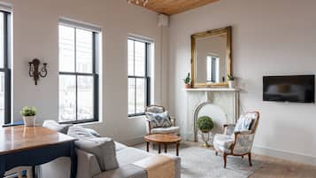 A living room with a wooden ceiling, large windows, a fireplace, a TV, and a sofa.