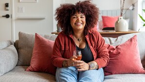A person sitting on a grey sofa with red cushions, holding a glass. - Brewery Park Hotel (Halifax)