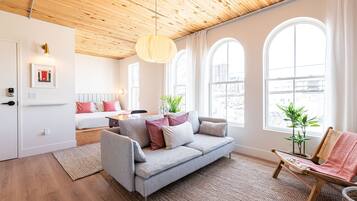 A modern living room with a wooden ceiling, a grey sofa, a wooden chair, and large windows.