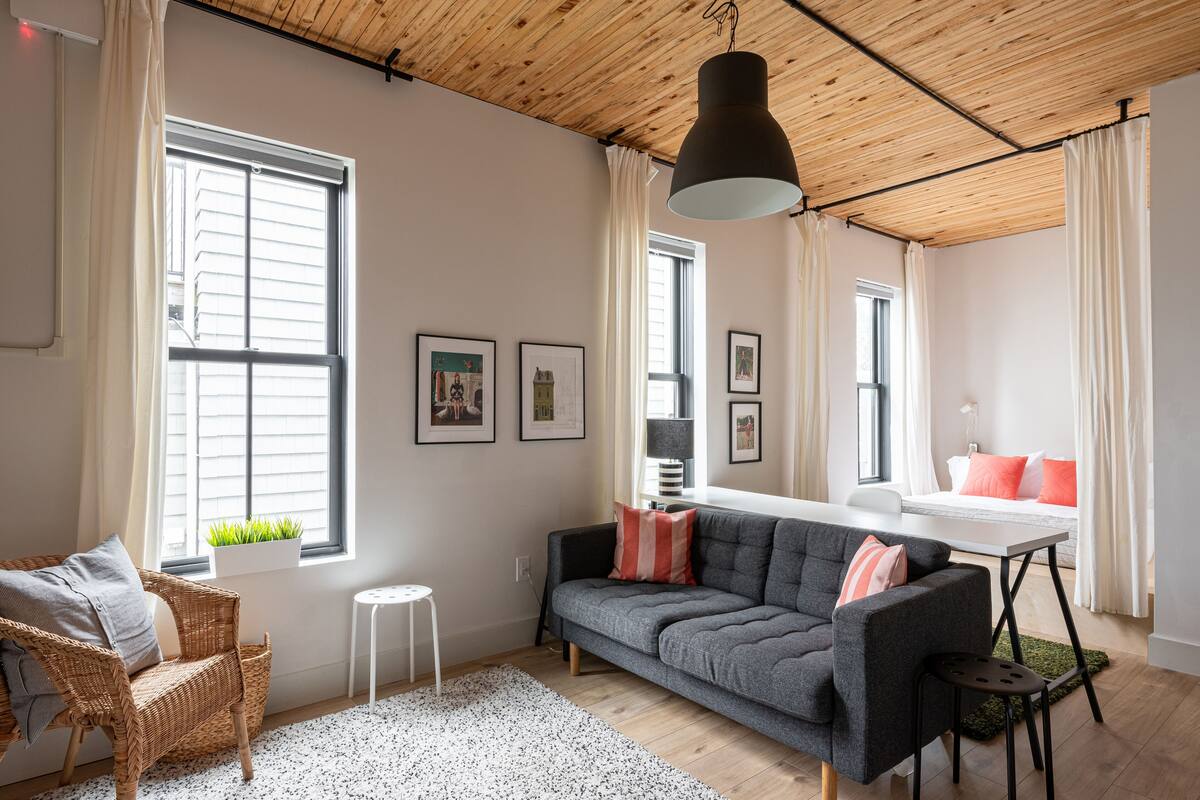 Una sala moderna con un sofá gris, una silla de mimbre, una mesa de comedor y una lámpara colgante.