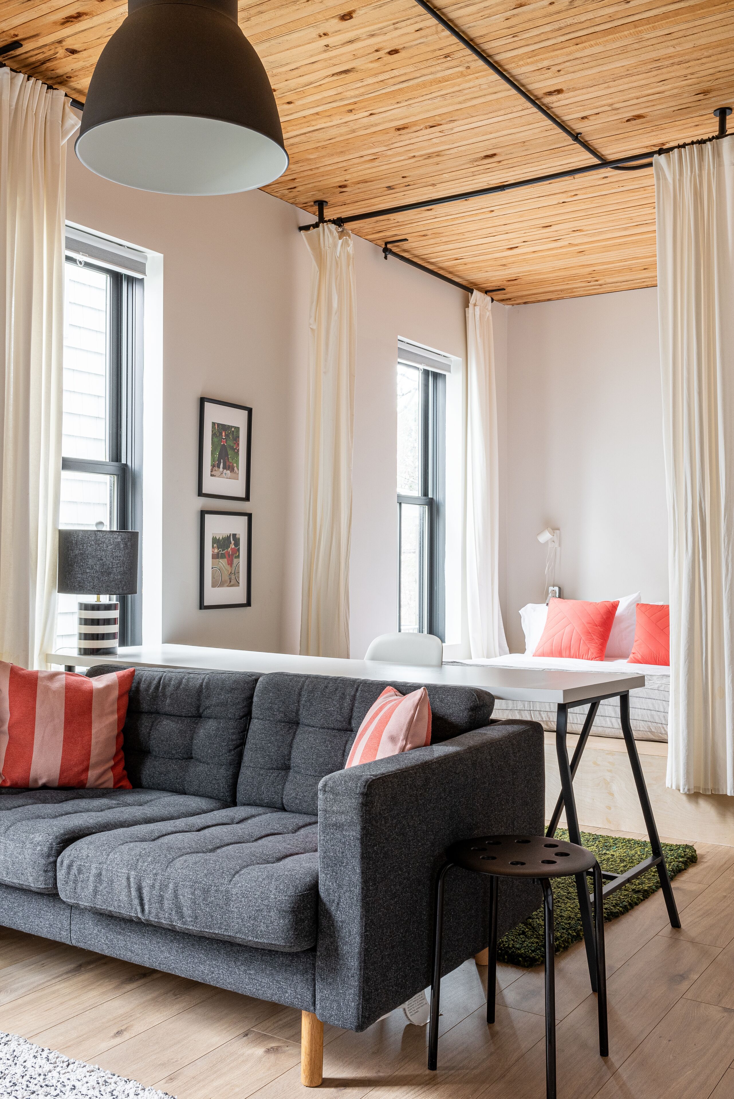 A modern living room with a grey sofa, a black chair, and a wooden ceiling.