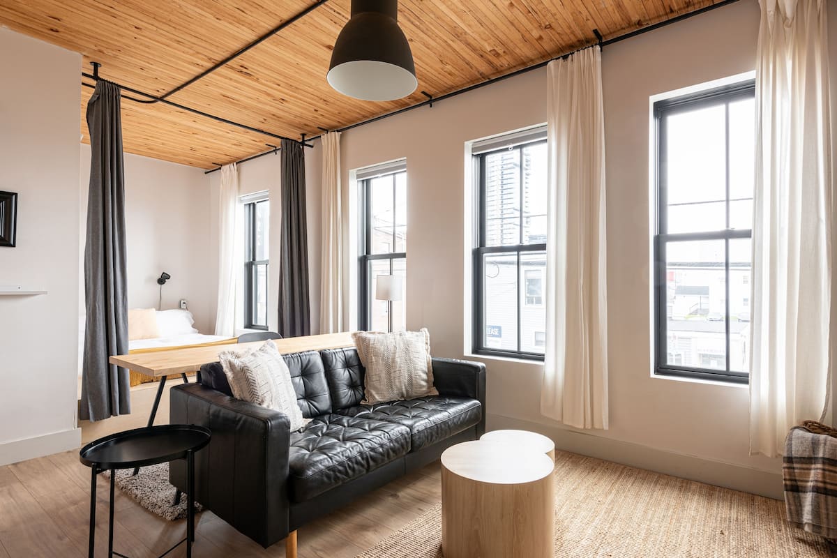 Una sala de estar moderna con un sofá de cuero negro, una mesa de centro redonda de madera y techo de madera.