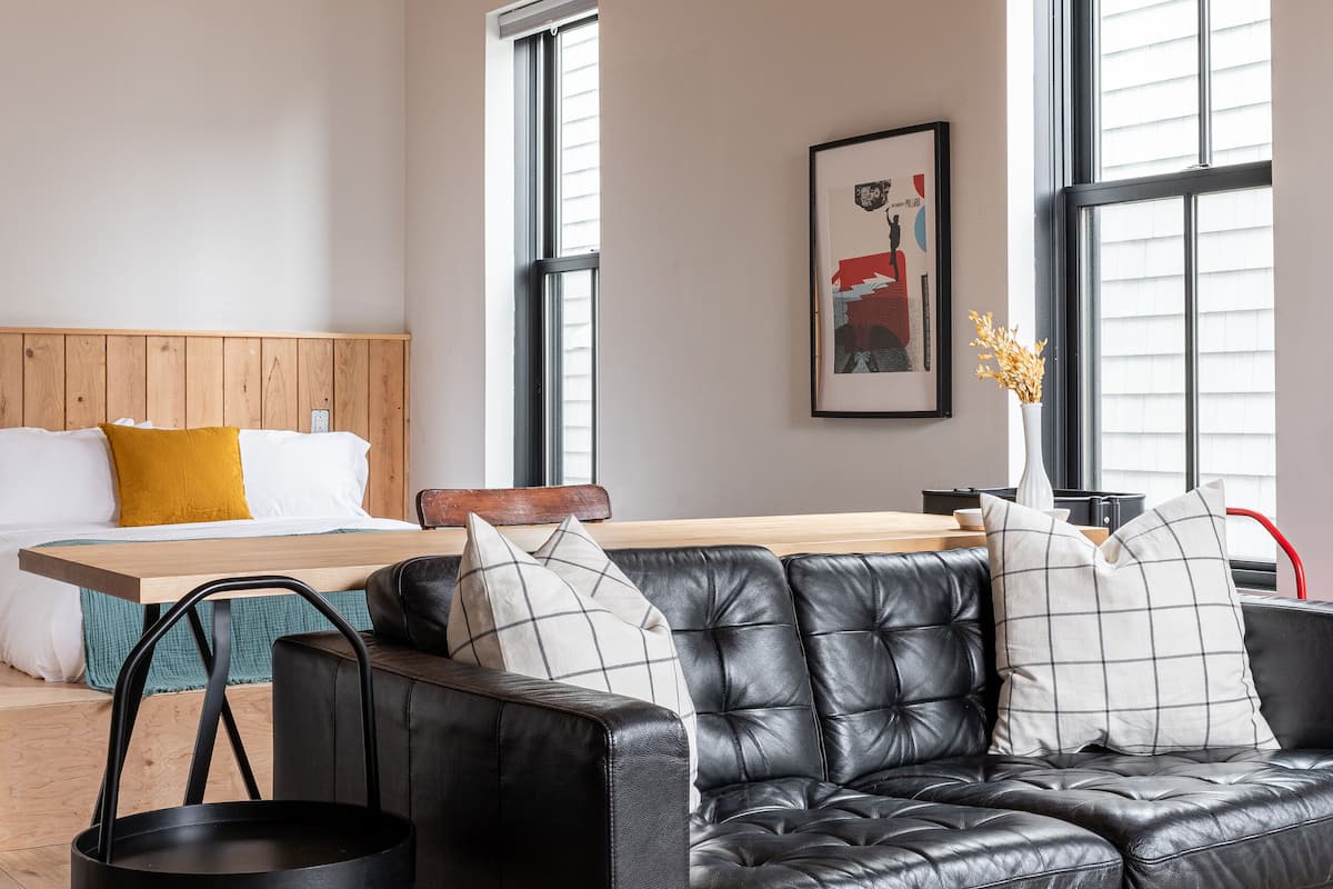 Una sala de estar moderna con un sofá de cuero negro, techo de madera y ventanas grandes.