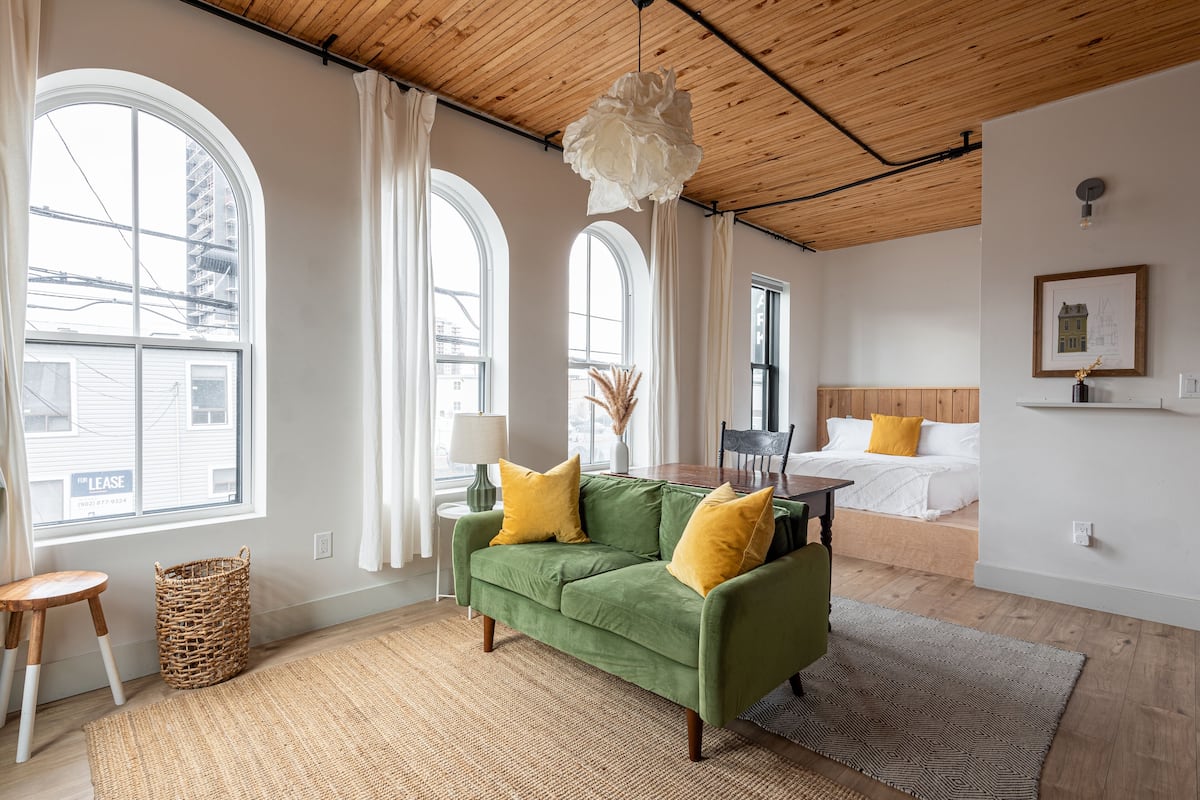 Una habitación con sofá verde, cama y ventanas amplias.