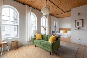 Una habitación con sofá verde, cama y ventanas amplias.