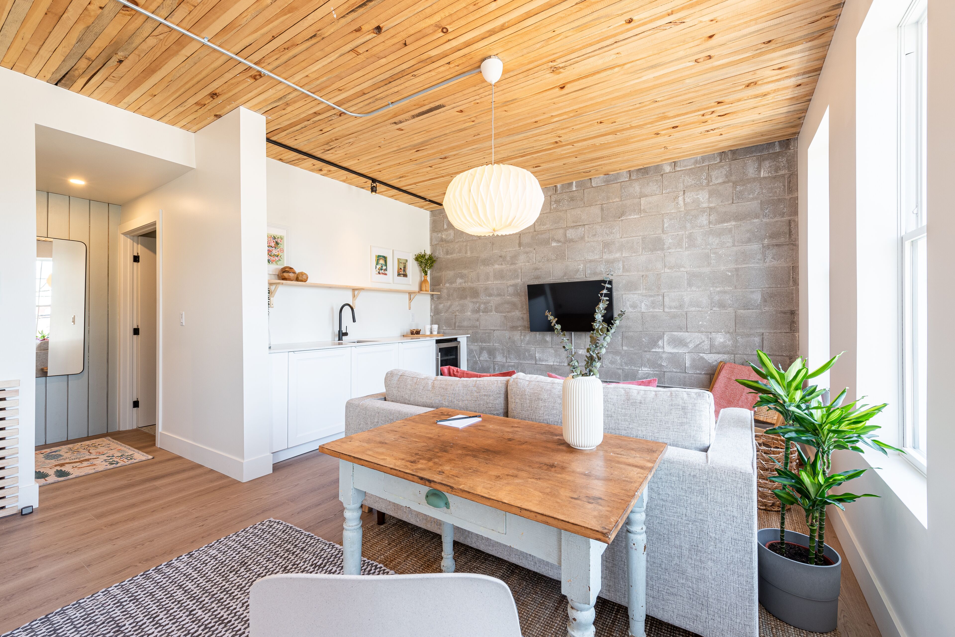 Un soggiorno moderno con soffitto in legno, un divano grigio, un tavolino in legno e una TV montata su un muro in mattoni.