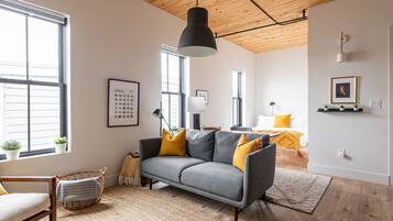 Una sala de estar moderna con un sofá gris, cojines amarillos, un sillón de mimbre y un ventanal grande.