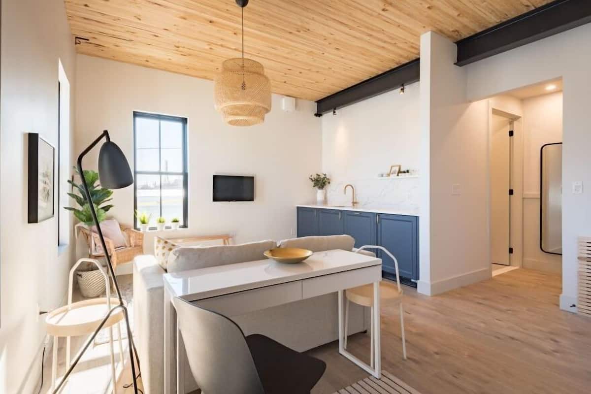 Una cocina moderna con armarios blancos, una zona de comedor con mesa y sillas blancas, y un ventanal que proporciona luz natural.