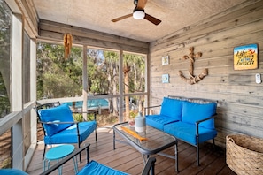 A covered outdoor seating area with blue furniture, a ceiling fan, and a view of a pool and trees. - Spacious condo enjoy Pool, Hot Tub access to Beach with Private Beach Locker ! (Hilton Head Island)
