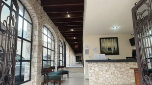 Um saguão de hotel com paredes de pedra, grandes janelas em arco, piso de madeira e um balcão de recepção.
