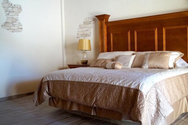 Una cama bien tendida con cabecera de madera, una lámpara de noche y un adorno de pared con diseño.