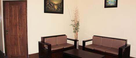 A room with a wooden door, two brown sofas, a coffee table, and two framed pictures on the wall.