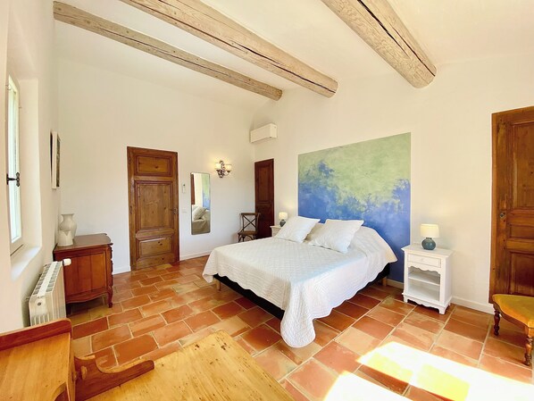 A bedroom with a large bed, a wooden floor, a mirror, and a painting on the wall. - Spacious, peaceful villa in 1 hectare grounds near Gordes (Goult)