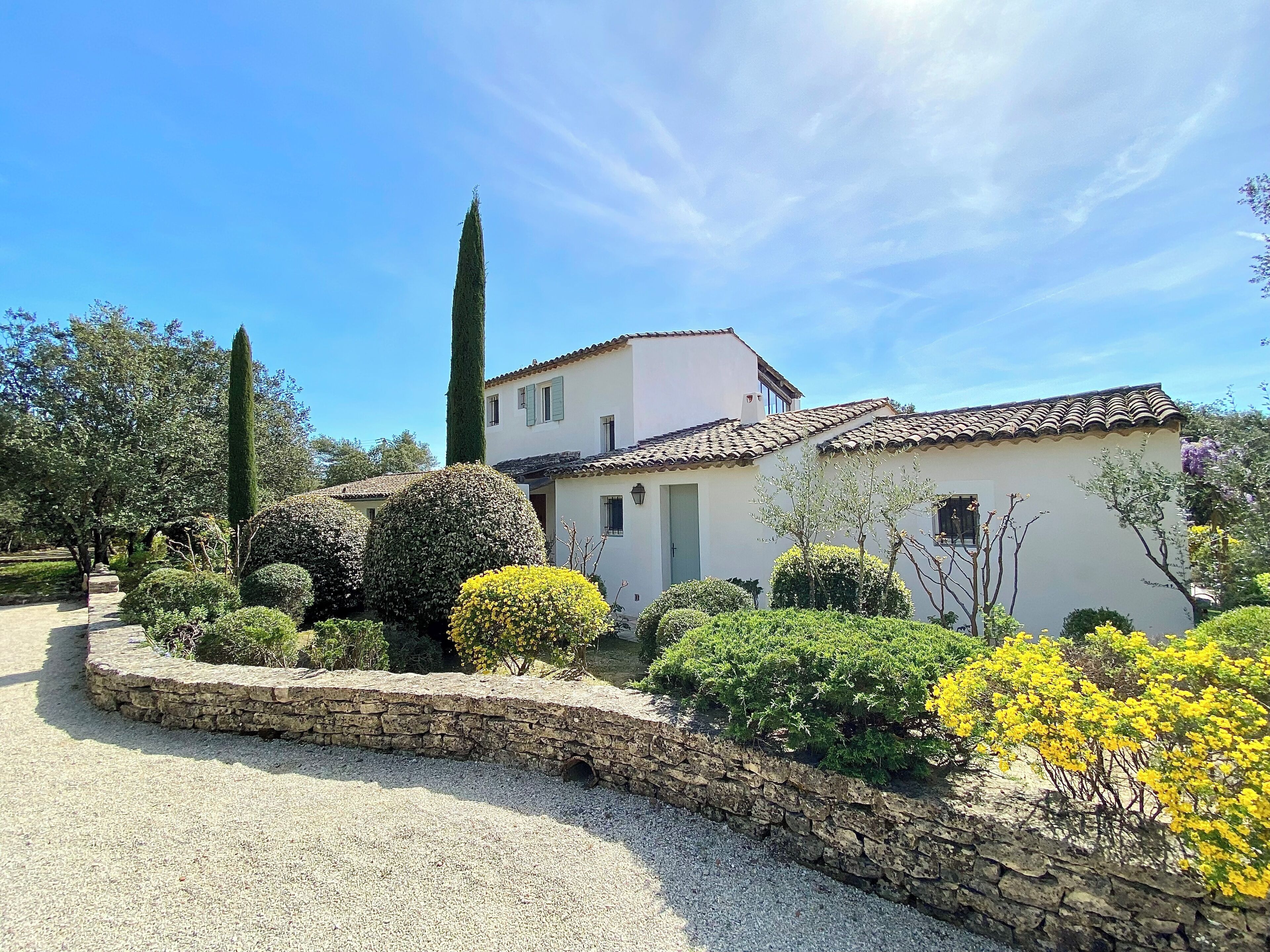 A white building with a tiled roof, surrounded by well-maintained gardens and a gravel path.