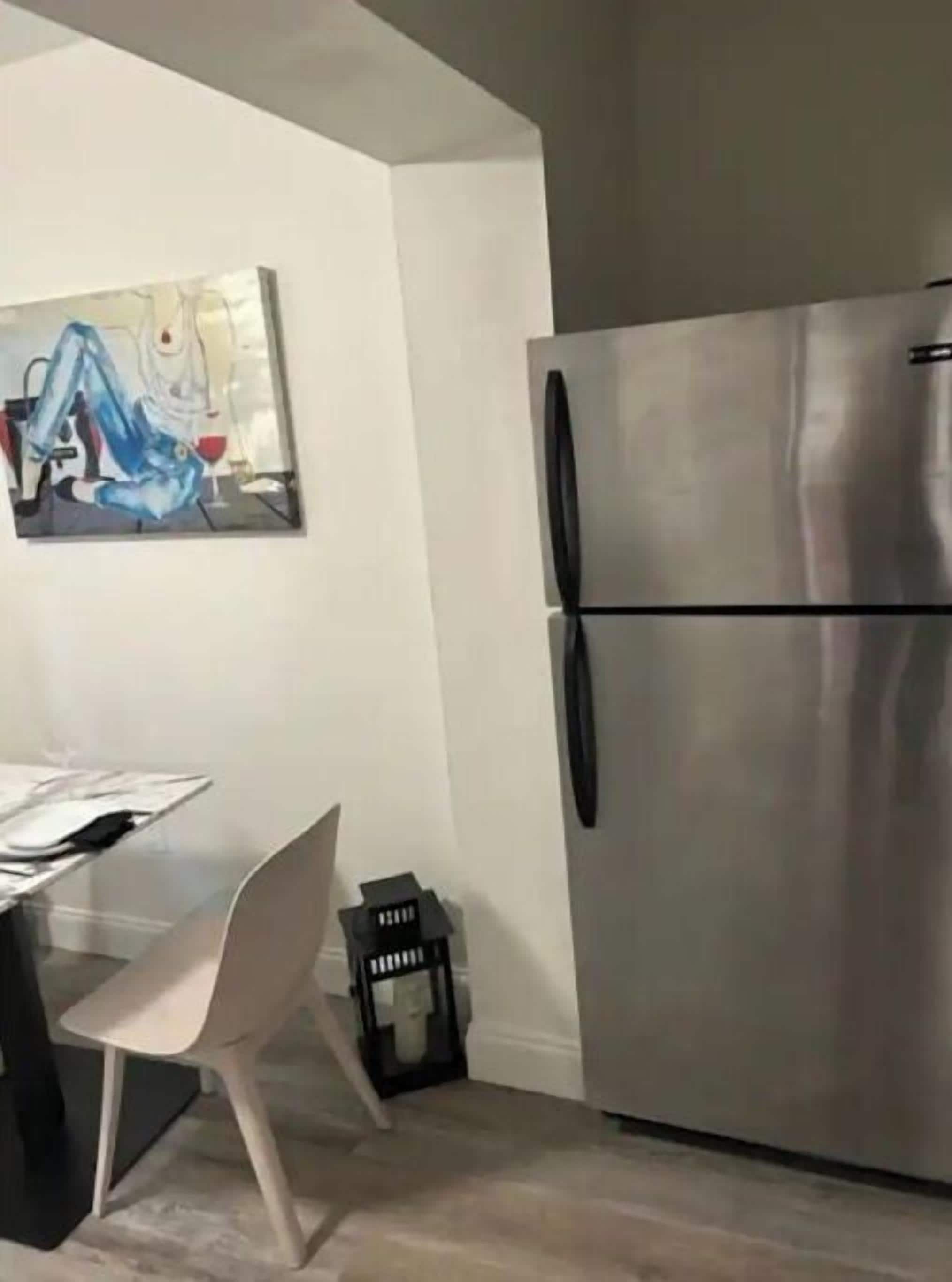 Una cocina moderna con un refrigerador de acero inoxidable, una mesa de comedor con sillas y un cuadro en la pared.
