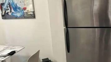 Una cocina moderna con un refrigerador de acero inoxidable, una mesa de comedor con sillas y un cuadro en la pared.