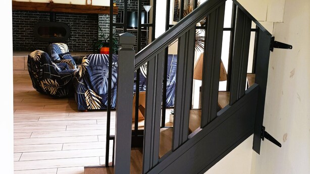 Un escalier avec une rampe noire et des marches en bois menant à l’étage supérieur.