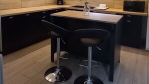 Une cuisine moderne avec des meubles en bois, un îlot central doté de tabourets, un éclairage suspendu et une fenêtre au-dessus de l’évier.