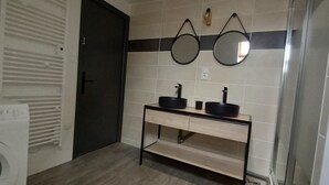 Une salle de bain équipée d’un lave-linge, d’un lavabo avec deux miroirs et d’une étagère.