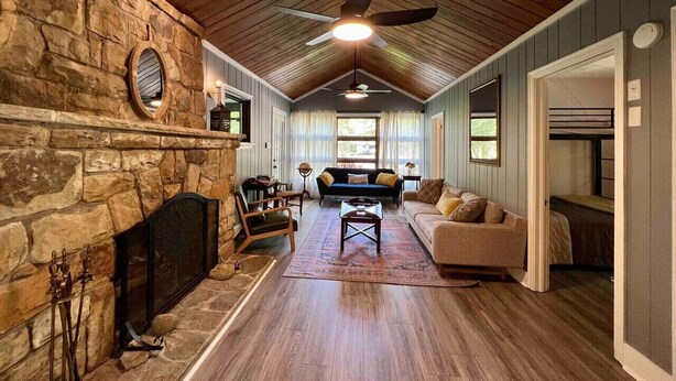 A cozy living room with a stone fireplace, wooden ceiling, and a comfortable seating area with a sofa and chairs.