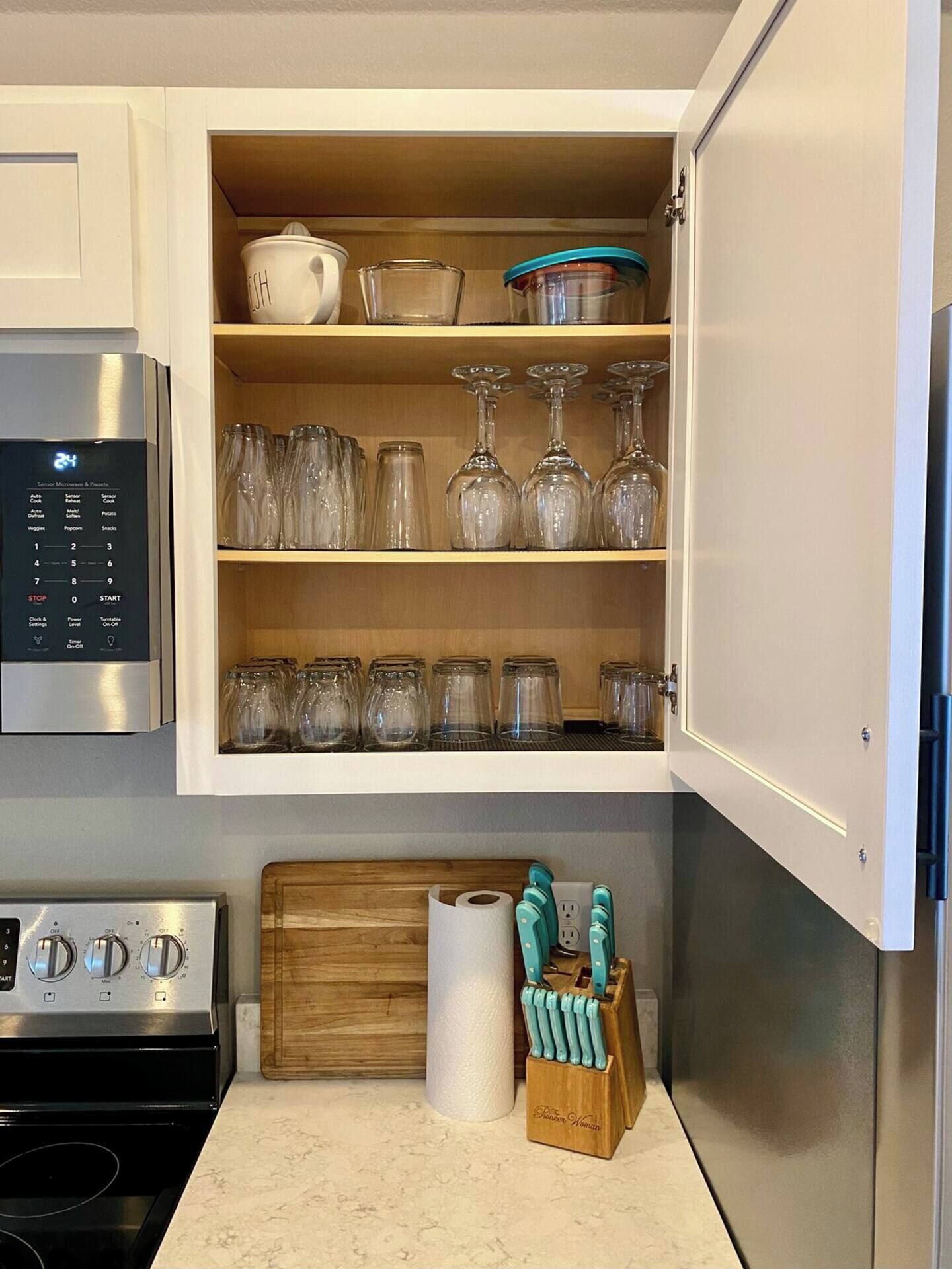 A kitchen with a built-in microwave, a stove, and a cabinet with glassware and jars.