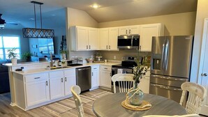 A modern kitchen with white cabinetry, stainless steel appliances, and a dining area with a round table and white chairs.