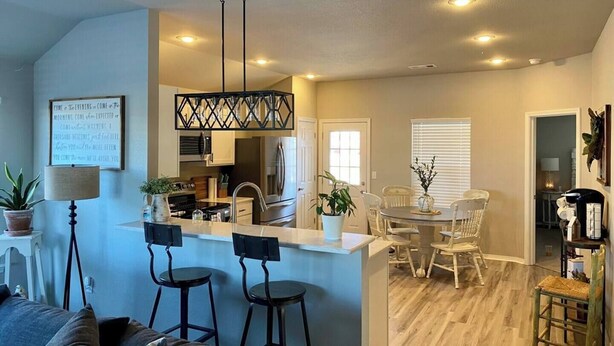 A modern kitchen with a central island, bar stools, and a dining area with a table and chairs.