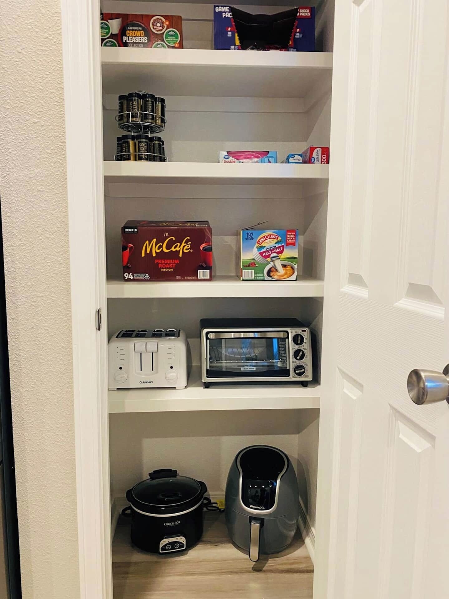 A kitchen pantry with shelves containing McCafé coffee, cereal, a toaster, a microwave, a slow cooker, and a kettle.