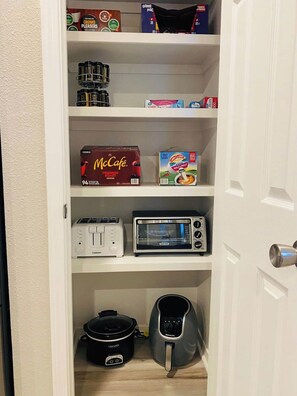 A kitchen pantry with shelves containing McCafé coffee, cereal, a toaster, a microwave, a slow cooker, and a kettle. - Charming Southern-style home with a signature red door and a Razorback game room—perfect for unwinding after a day in Fayetteville. (Fayetteville)