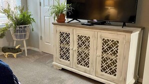 A living room with a television on a white cabinet, a door, and a window with blinds.