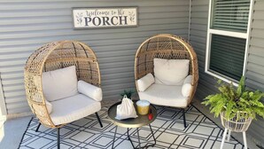 A porch with two wicker chairs, a small table, and a welcome sign.