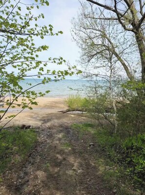 Un sentier de terre mène à une plage où la végétation et les arbres sont clairsemés.