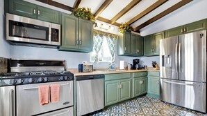 Una cocina con armarios verdes, electrodomésticos de acero inoxidable y baldosas de piso estampadas.