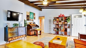 Una sala de estar con techo de madera, televisor de pantalla plana, piano, estantería y alfombra estampada.